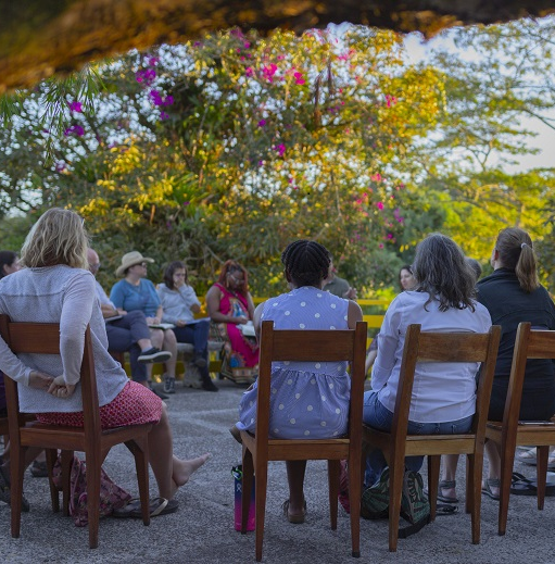People sit in a circle under a brightly colored tree.