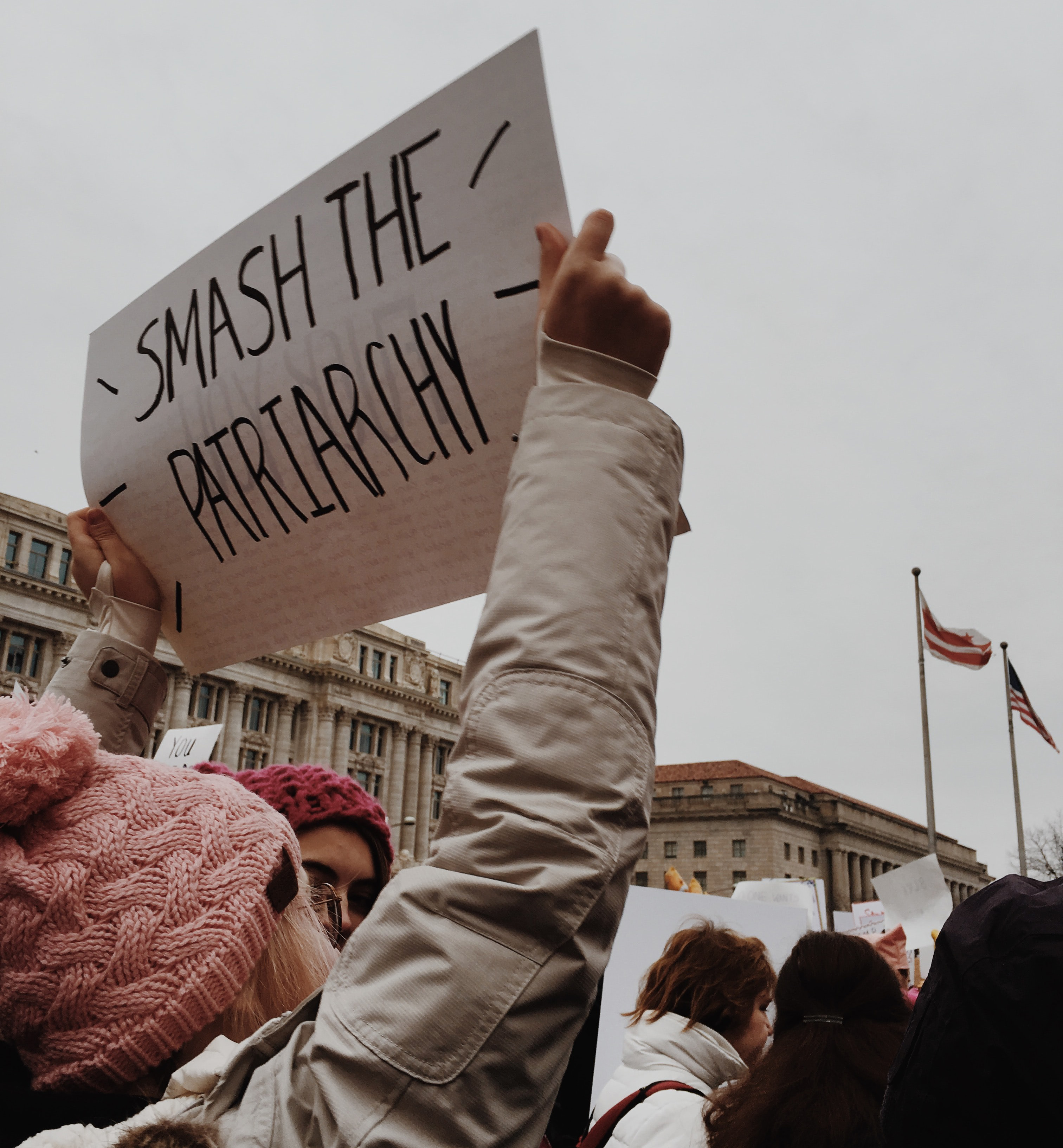 A person with a pink hat and beige jacket holds a sign that says 