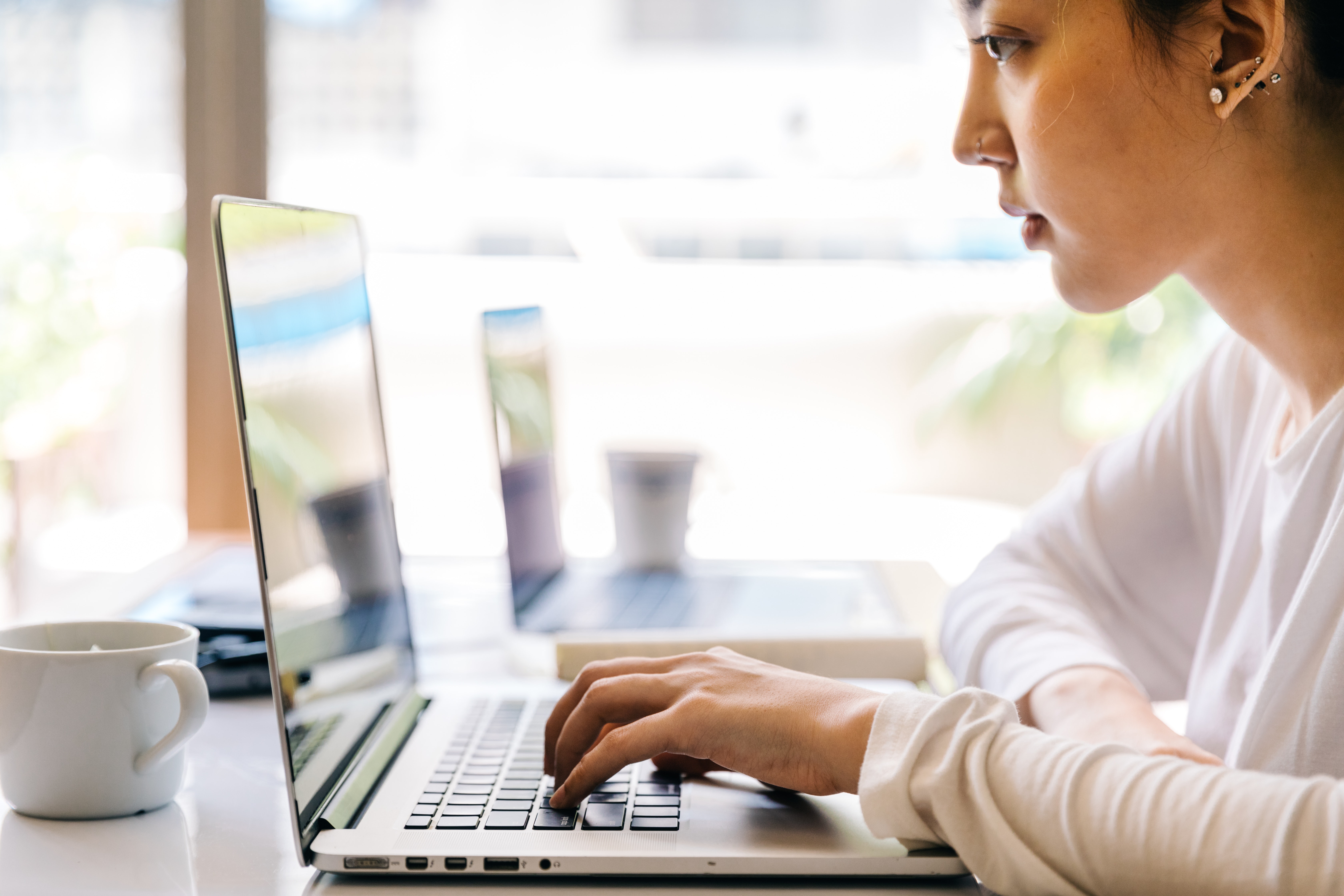 Individual wearing a white long sleeved shirt is poised in front of a laptop.