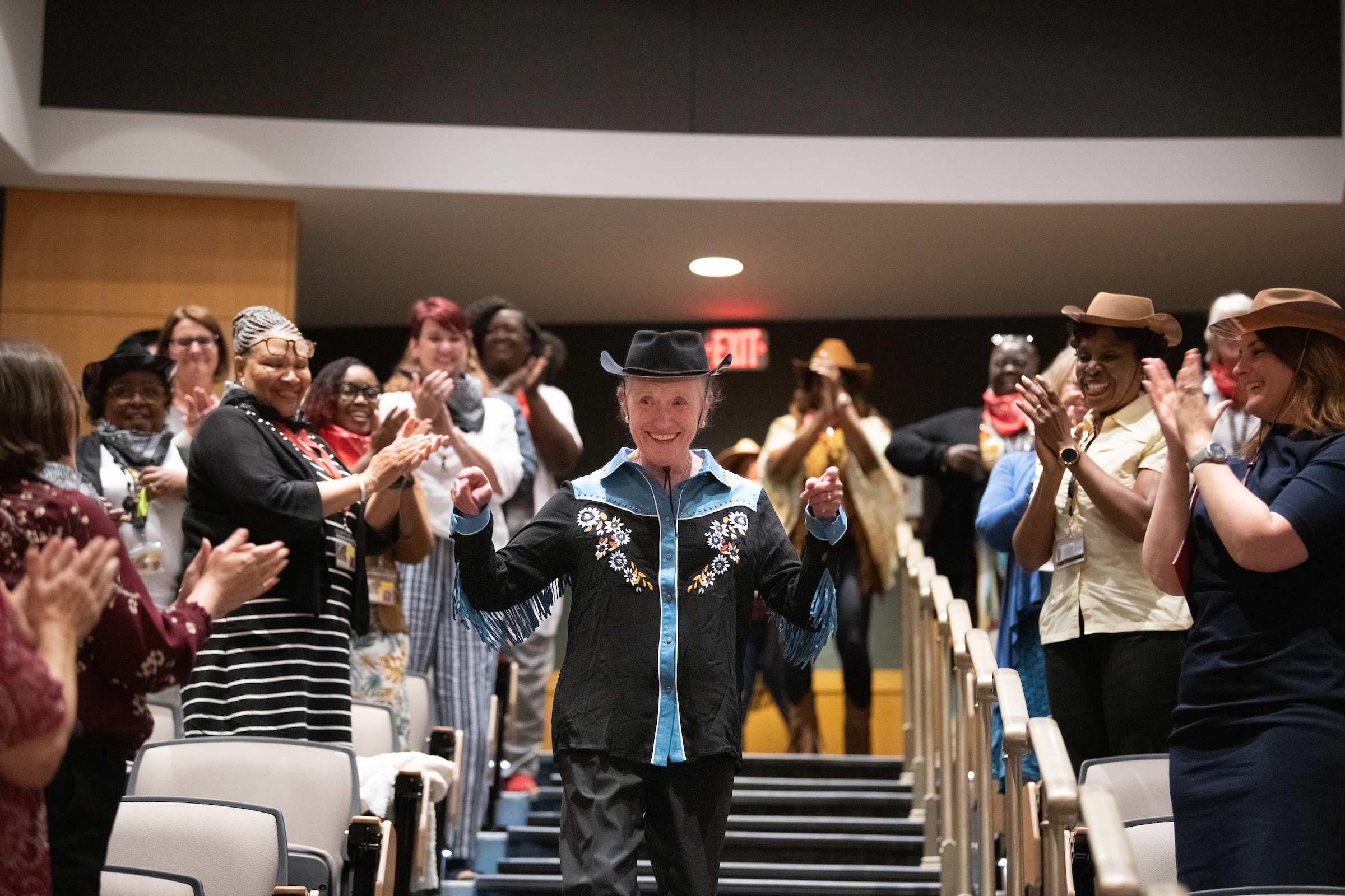 Dean Kirschling dressed in Western gear walking down stairs in auditorium with audience clapping