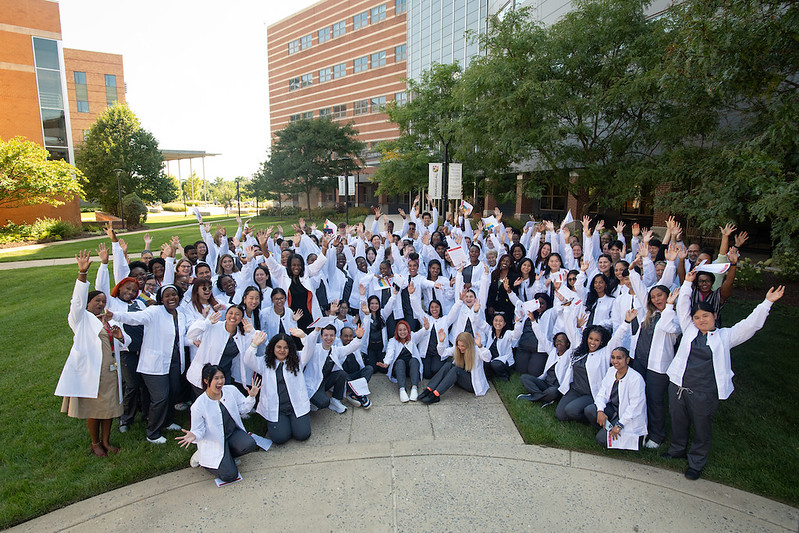 group photo of nursing students wearing gray scrubs and white scrub jackets in the USG courtyard