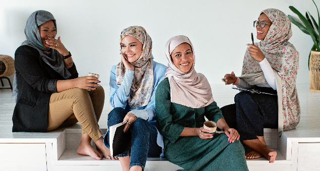 A group of four Muslim women with hijab sit together laughing.