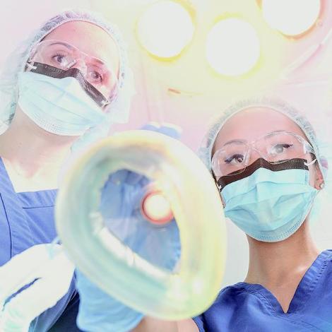 nurse anesthetists in caps and masks looking down at camera, holding anesthesia inhaler