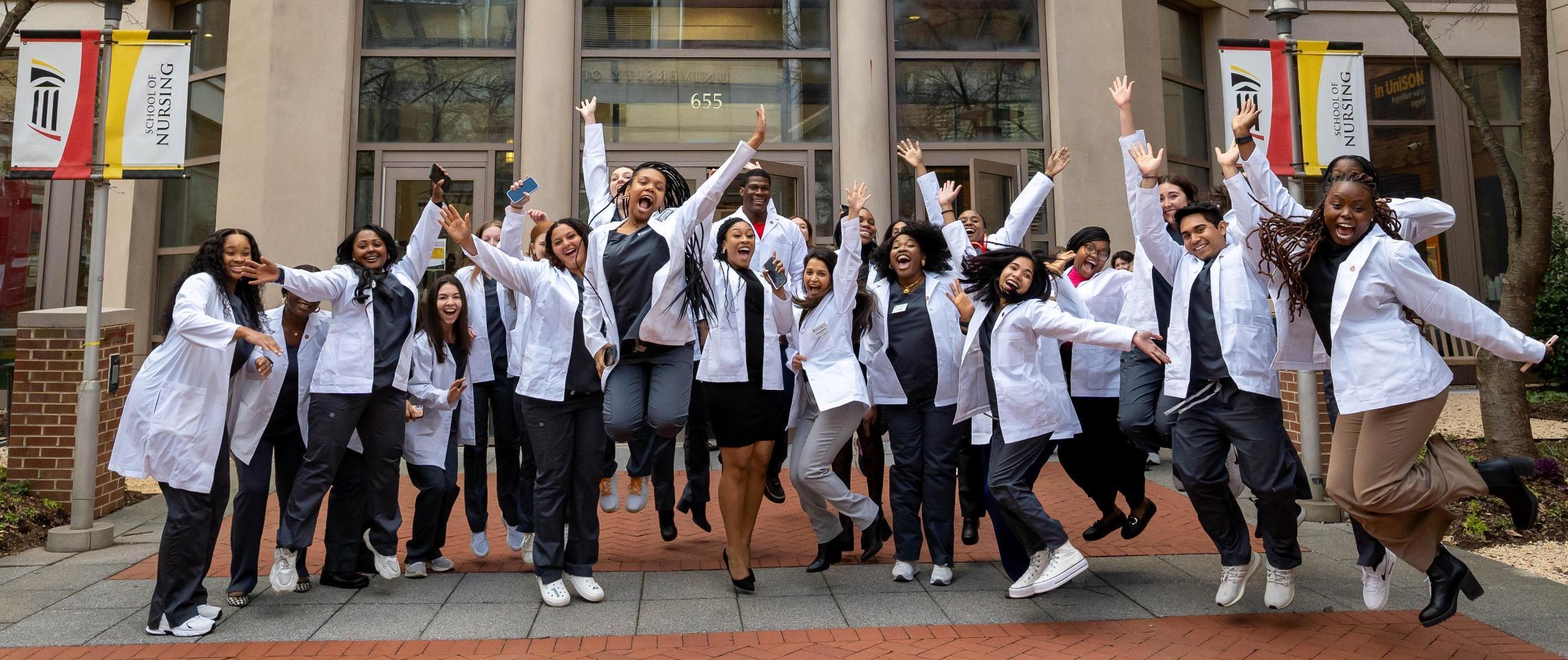 photo of students in white coats jumping in front of UMSON building 