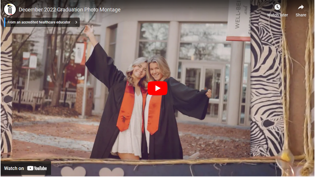 video still with play button, showing two graduates in regalia with arms around each other in front of School of Nursing building