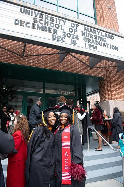 Graduates in regalia posing below Hippodrome marquee announcing UMSON December 2024 Graduation