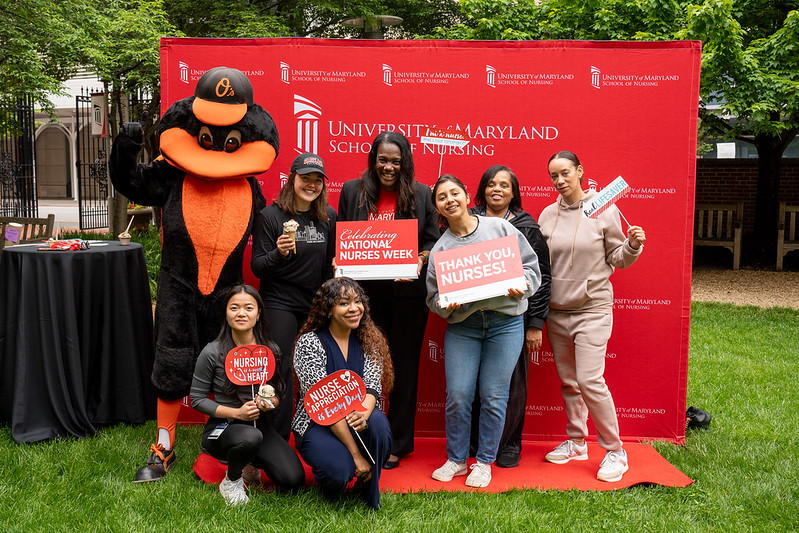 students with Dean Ogbolu and Oriole Bird in front of step and repeat with Nurses Week photo props