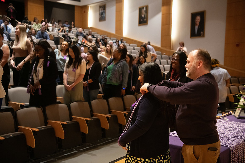 photo of student being corded by Pi at-Large Chapter president Paul Thurmann, with Dean Ogbolu in background