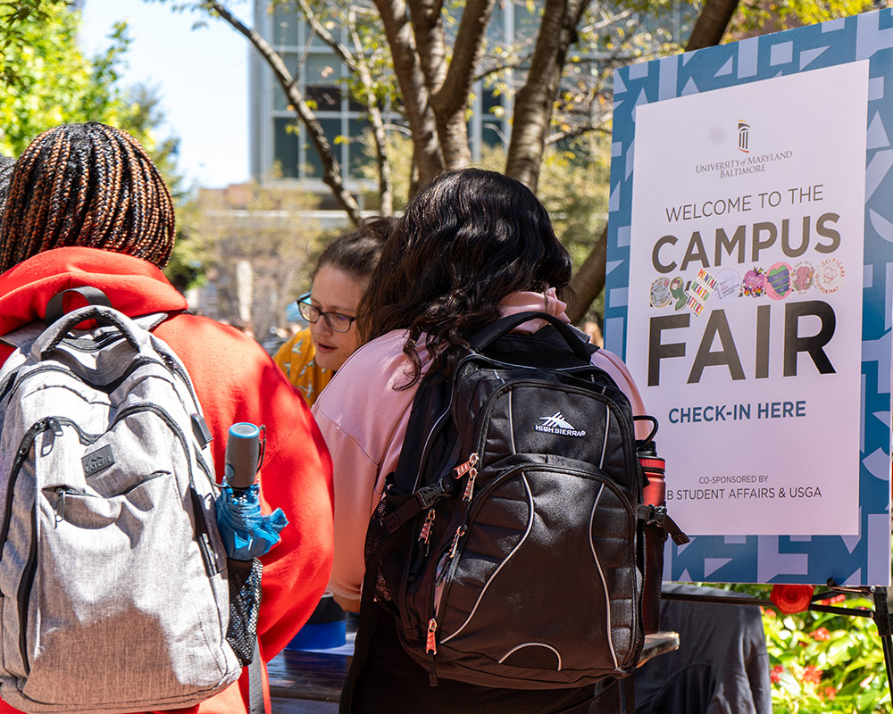 Students standing outdoors a table next to a sign with that reads 