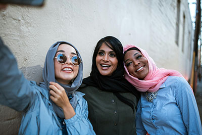 Three Muslim women smiling while taking a selfie photo together.