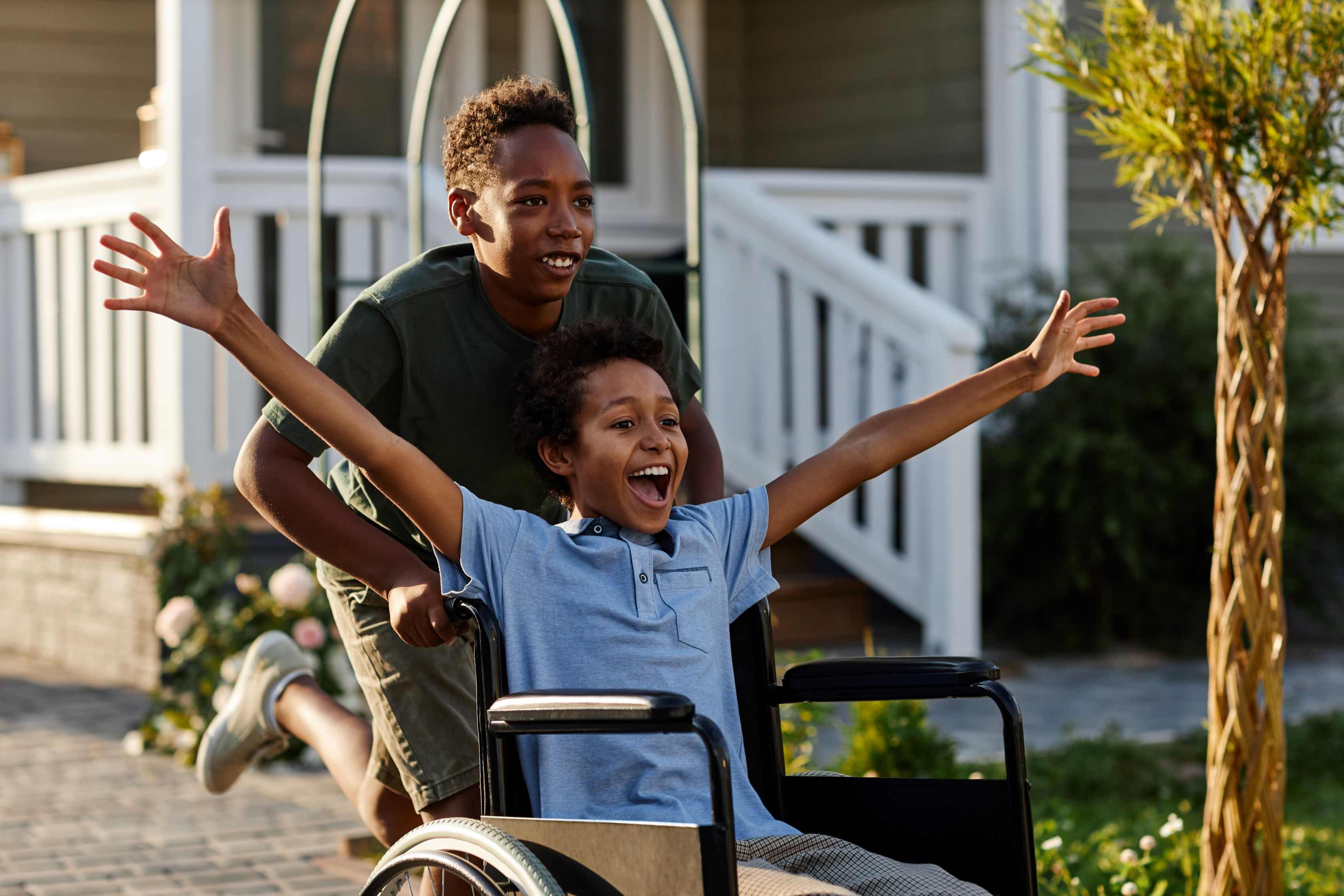 smiling child in wheelchair with arms spread wide and woman pushing the chair