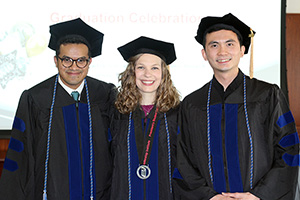 Three PhD graduates in cap and gown