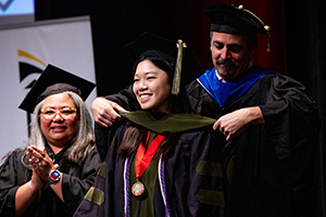 A student receives their hood at the PharmD graduation ceremony.