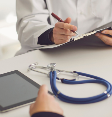 person with white coat on, holding clipboard pen, opposite another with tablet and stethoscope on table