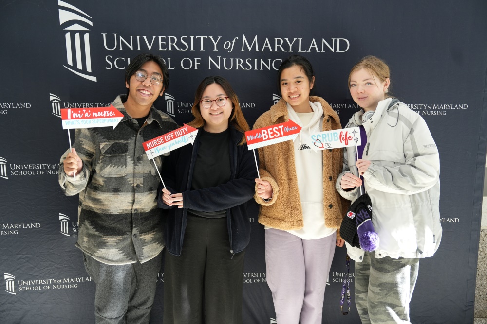 students posing with selfie props in front of a black step and repeat wtih the UMSON logo