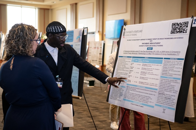 Student pointing to poster project while standing next to faculty member who is looking at the poster