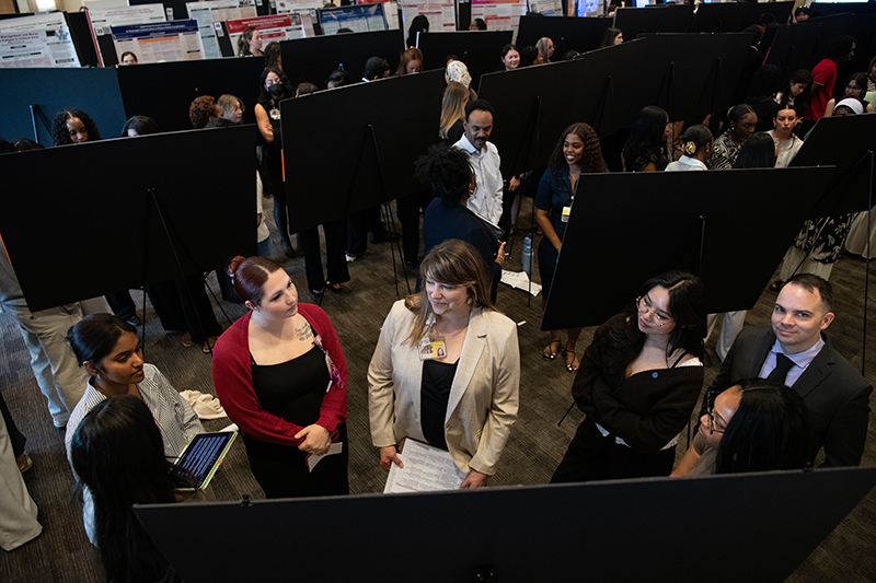 A group of students engaged in conversation at Poster Day. Posteres surround them, creating a lively, collaborative atmosphere.