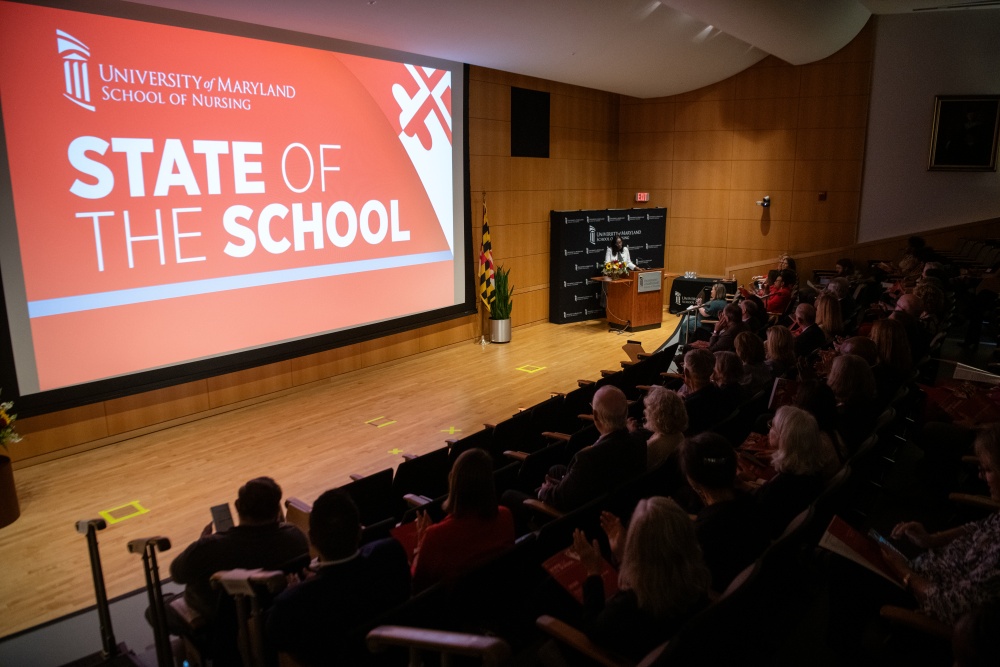 Audience members listen as Dean Ogbolu stands at a podium beneath a “State of the School” presentation at the University of Maryland School of Nursing.
