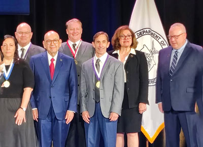 C. Daniel Mullins, centered, poses with fellow recipients at an award presentation, with medals visible and a department banner in the background.