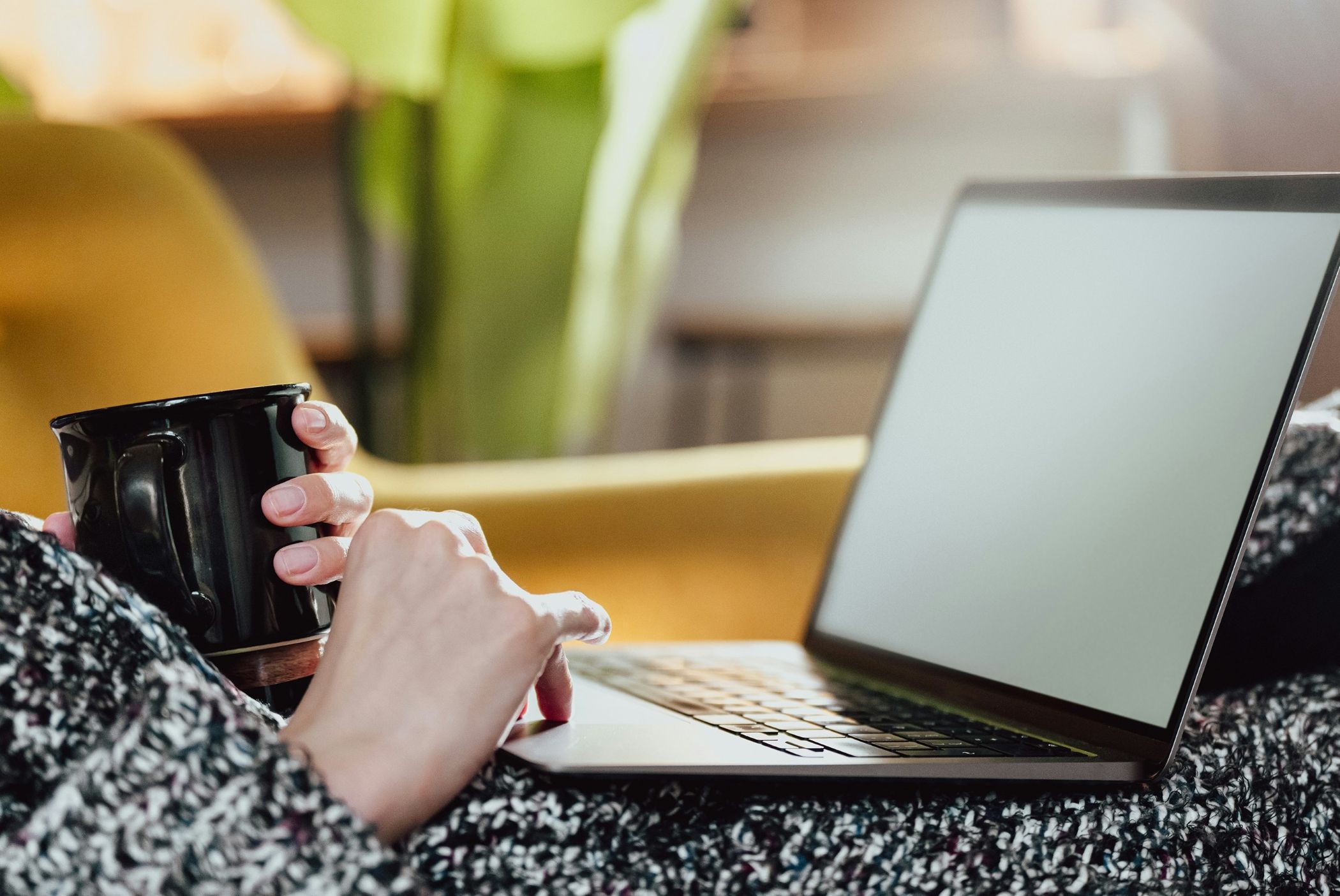 Person sitting comfortably with a laptop, holding a mug while typing, suggesting a relaxed online working or learning environment.