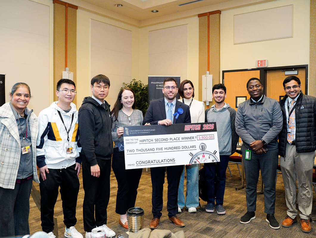 Athanasios Chamzas holds a HiPitch second‑place check while posing with members of the University of Maryland School of Pharmacy community at the HiPitch finals.