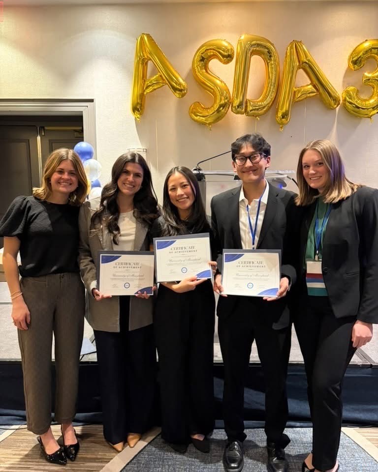 students holding paper certificates with balloons spelling ASDA behind them 