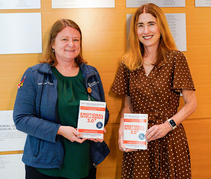 Megan Ehret and Dean Sarah Michel stand together holding copies of the book Emotional Intelligence 2.0.
