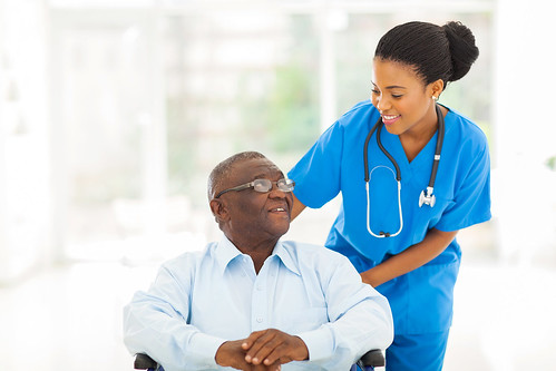 Health care professional and adult patient in a wheelchair smiling at each other.