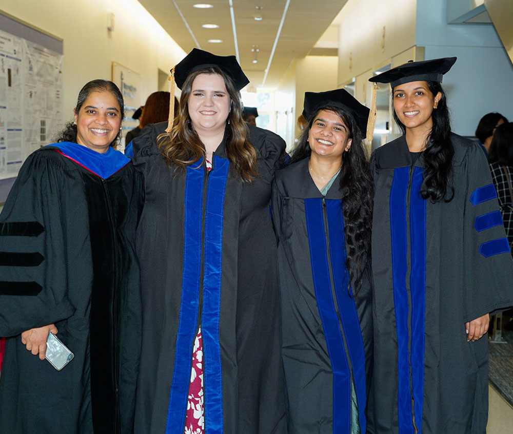 Mathangi GopalKrishnan, Brooke Langevin, Roshni Patel and one other PhD in PSC graduate stand in HSF II in academic regalia at the PhD in PSC graduation celebration.
