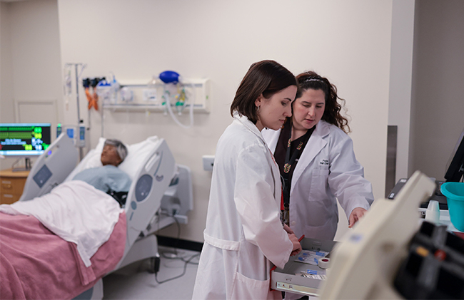 Nursing students in white coats working at a computer in a simulation lab