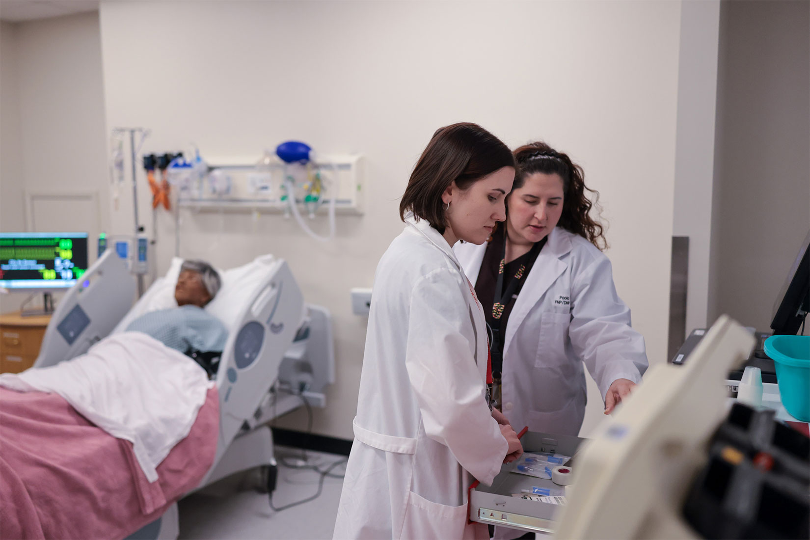 Two nursing students wearing white coats at a computer in a simulation lab