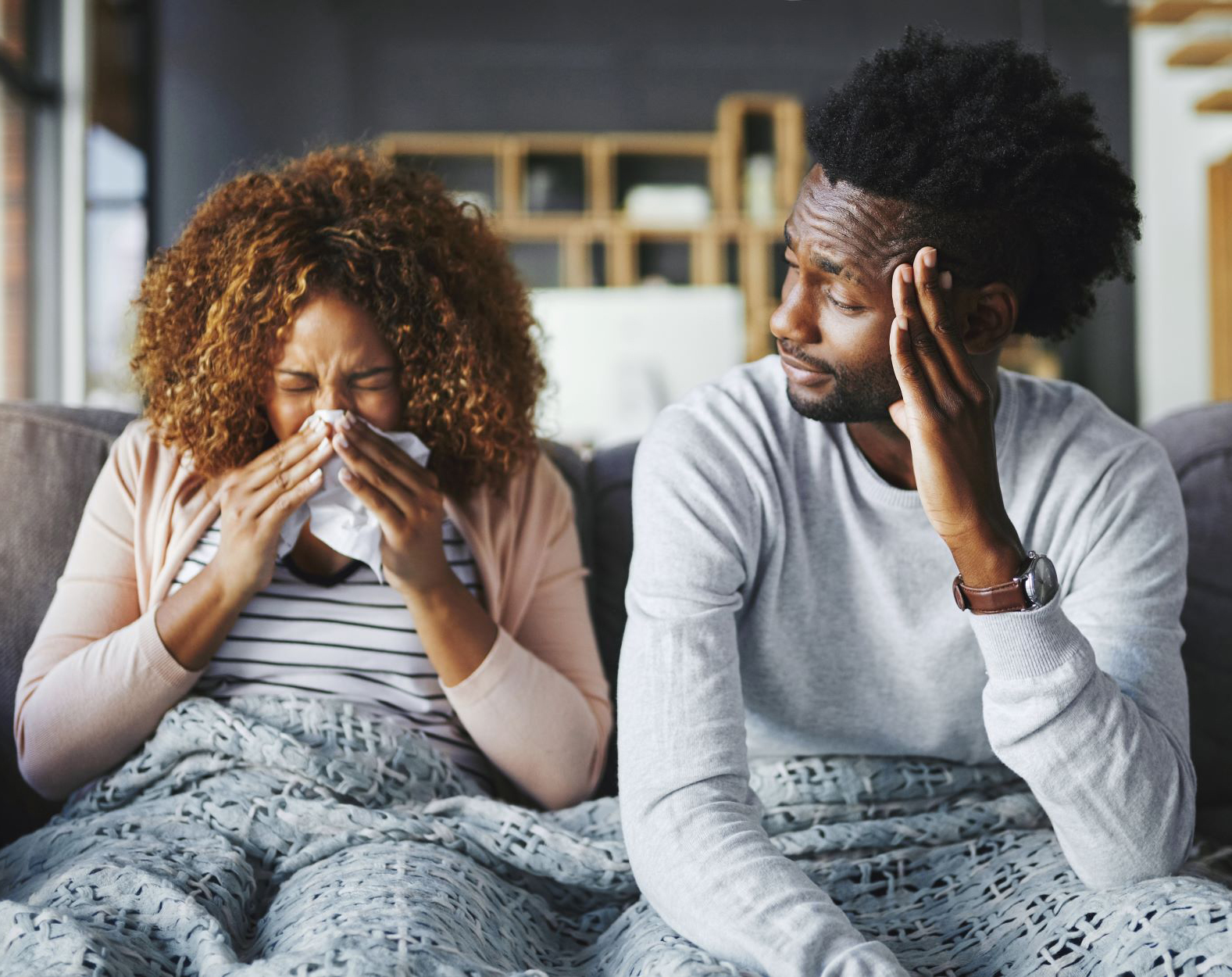 Woman sneezing with man sitting next to her