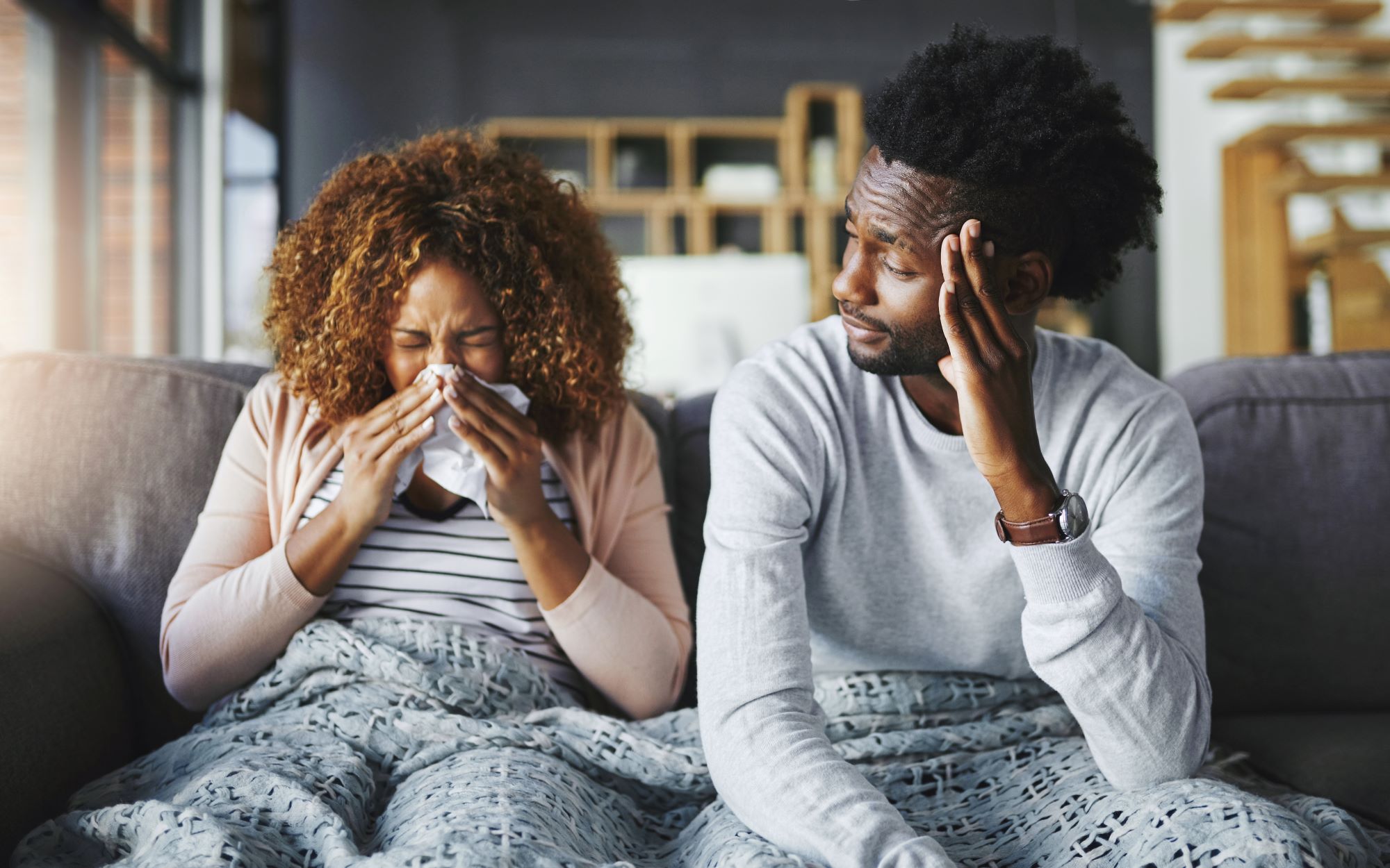 Woman sneezing with man sitting next to her