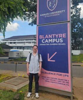 A student stands in front of a sign for Kamuzu University.