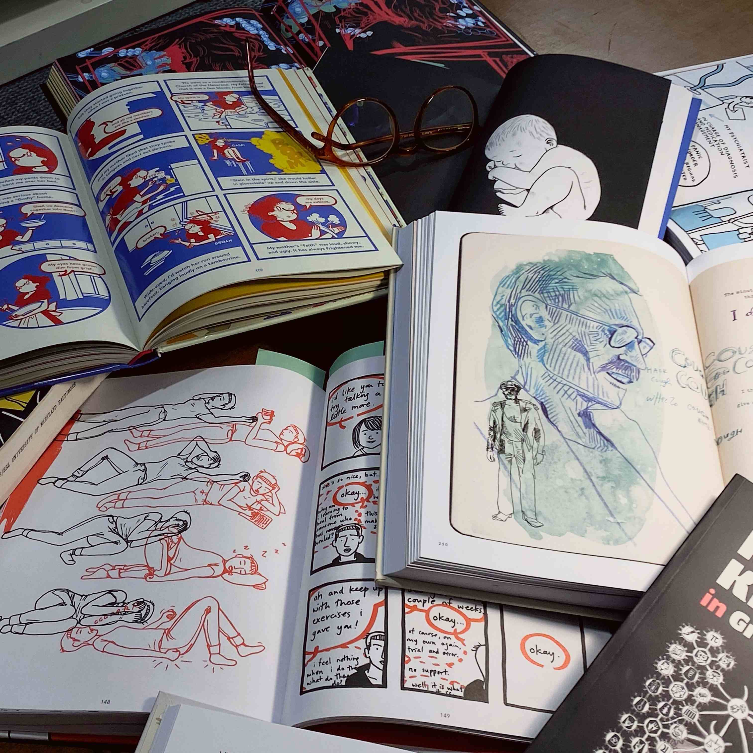 Image shows many books of graphic medicine illustrations scattered on a table