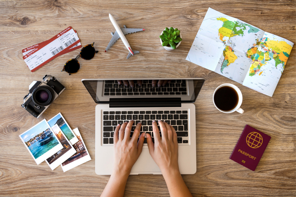 laptop on table surrounded by coffee, map, sunglasses, camera