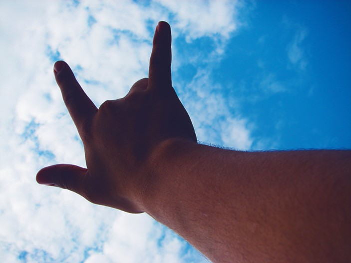 hand raised to the sky with clouds in background signing 