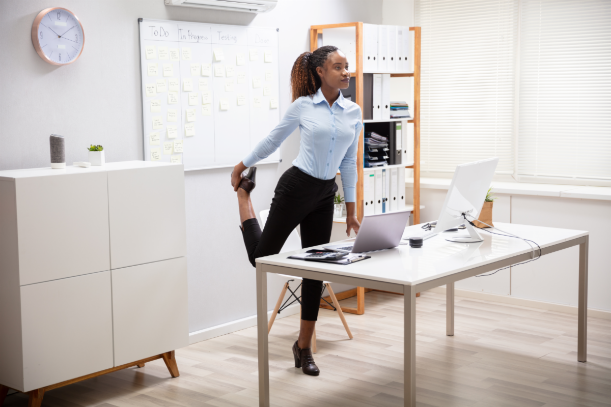 image of woman standing up and stretching her leg at a desk in an office space