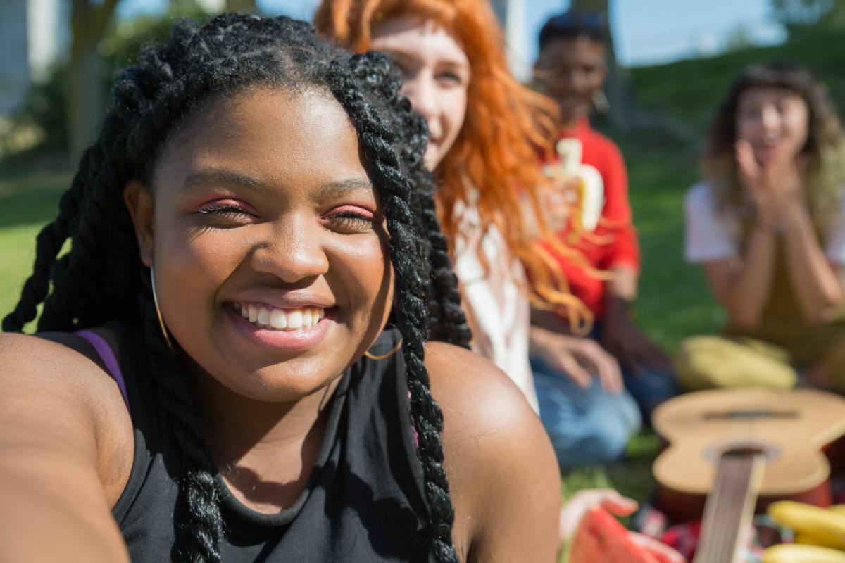 A smiling person sitting outdoors with individuals smiling behind them.