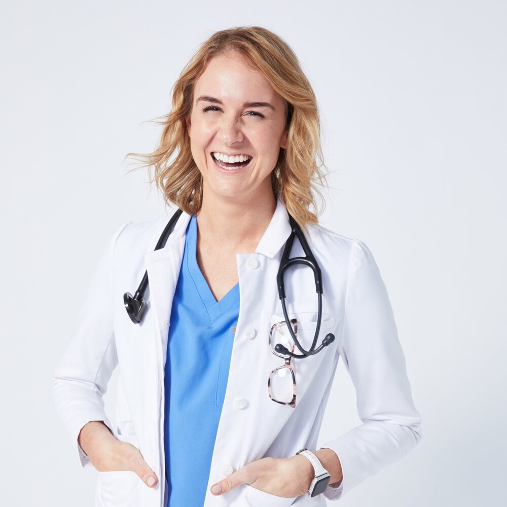 Danielle LeVeck wearing blue scrubs and a white lab coat with a stethoscope around her neck.