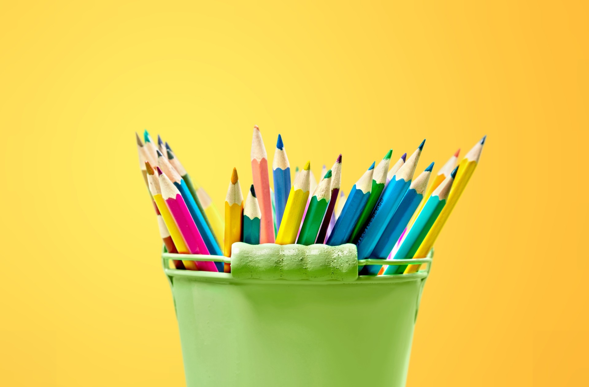 Green bucket with color pencils on yellow background