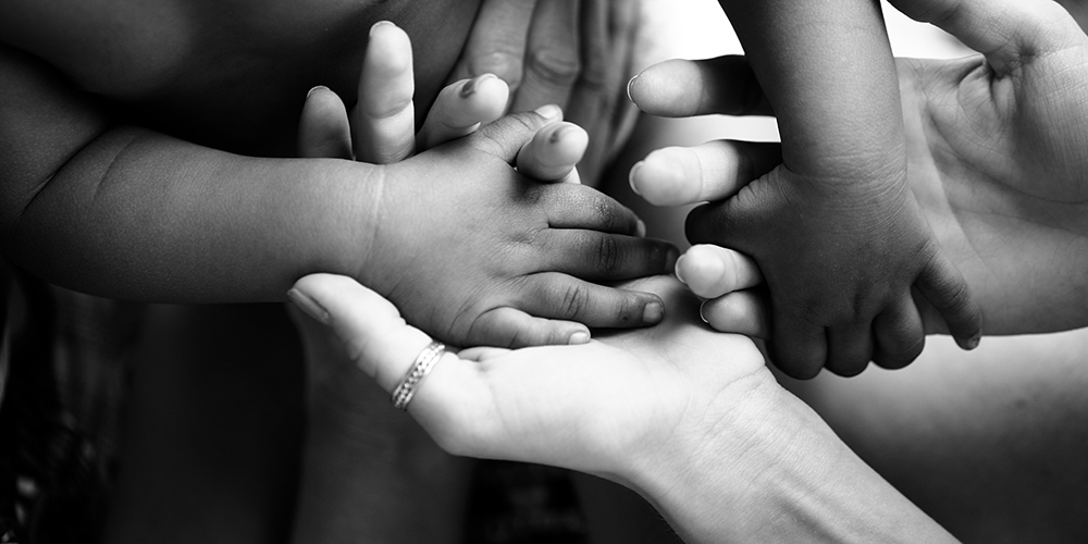 brown baby hands interlocked with white adult hands