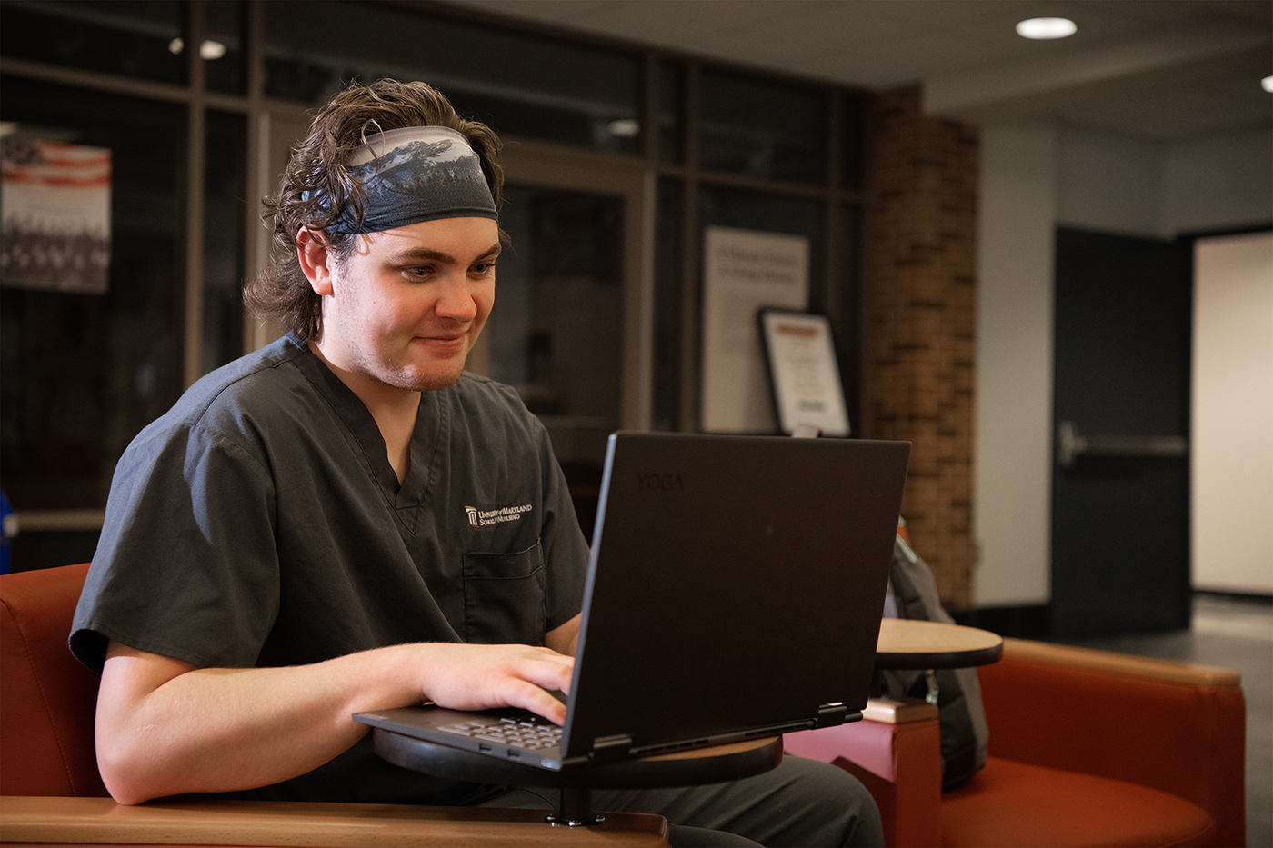 student in gray UMSON scrubs using laptop
