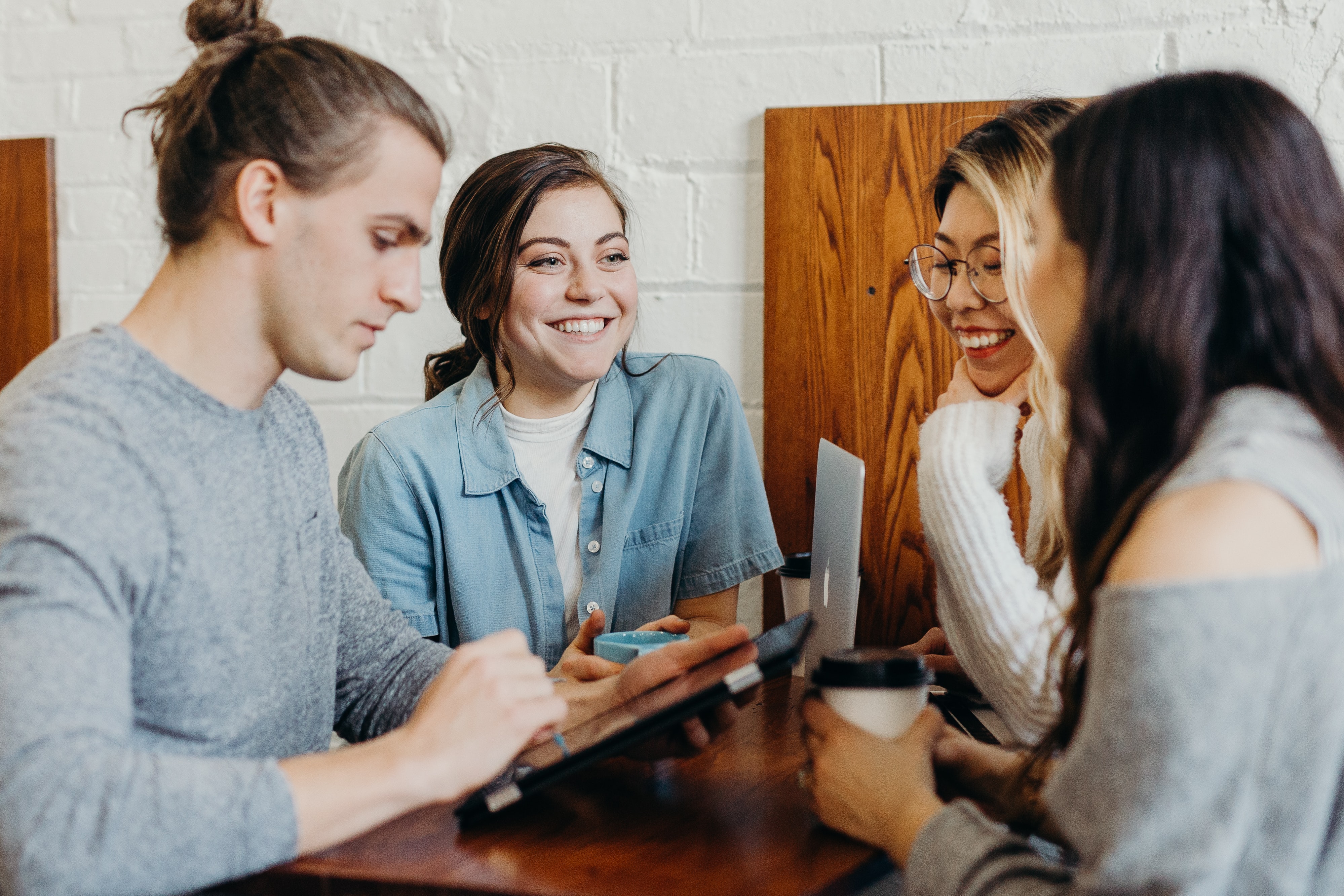 Four individuals sit at a wooden table. They are smiling at one another.