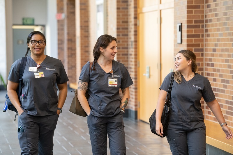 Three students in gray UMSON scrubs walking through a nursing building corridor
