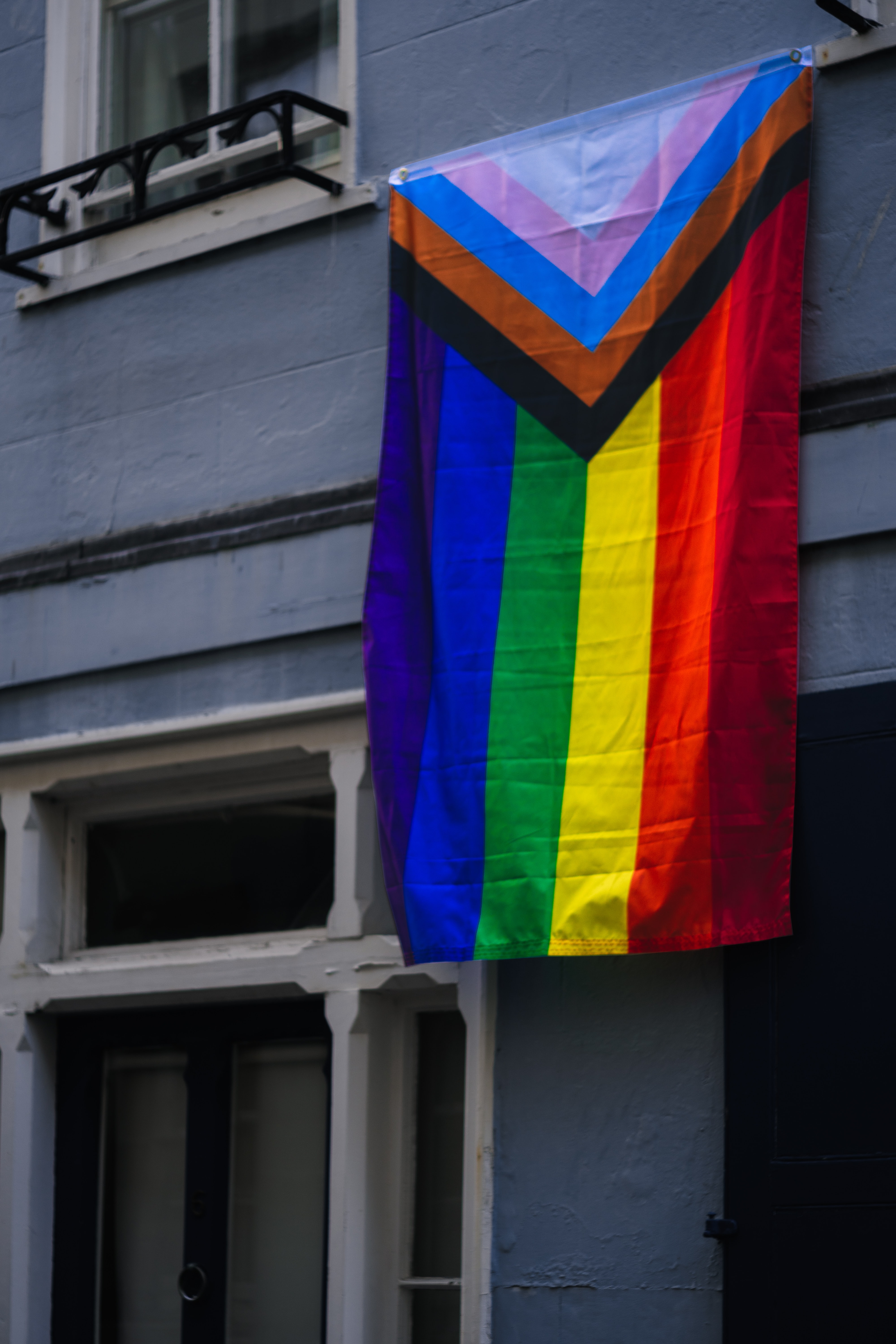 LBGTQ+ flag hanging on the exterior wall of a building.