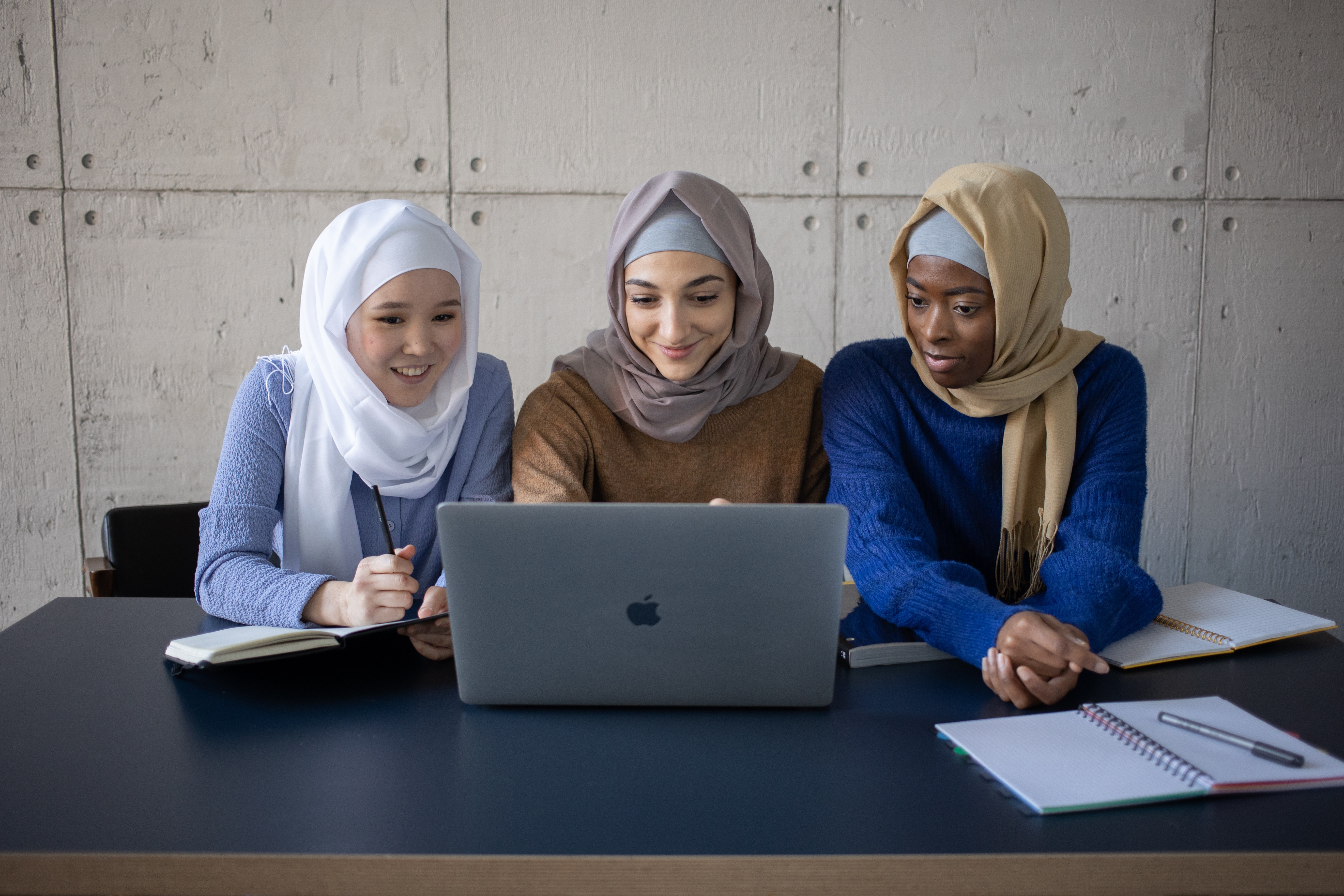 Three individuals wearing hijab sit in front of a laptop.