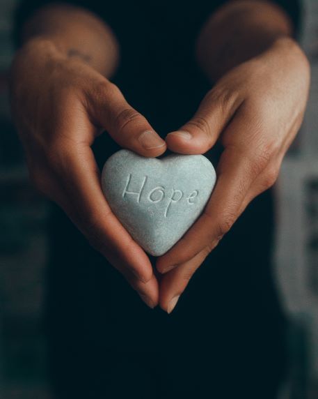 Hands holding heart-shaped rock with 'hope'