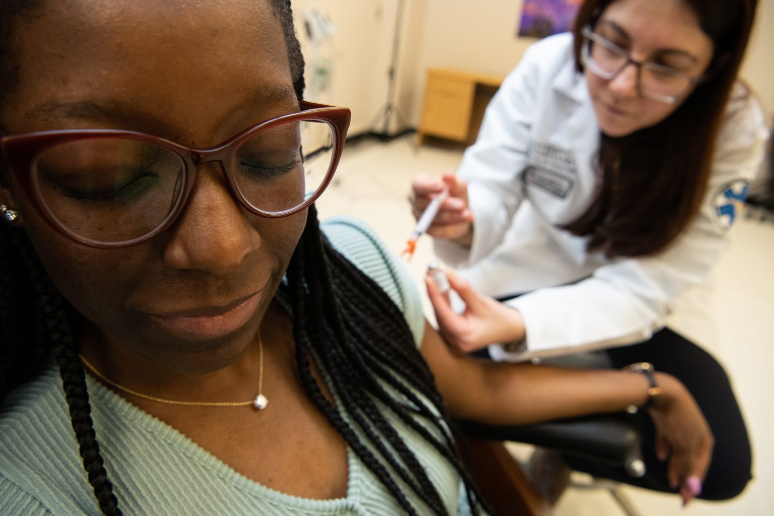 Woman looks away as doctor prepares to give her a shot.