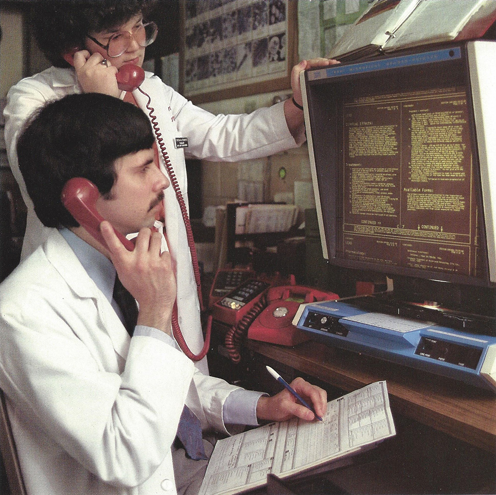 a man and a woman on phones while looking at computer screen circa 1980